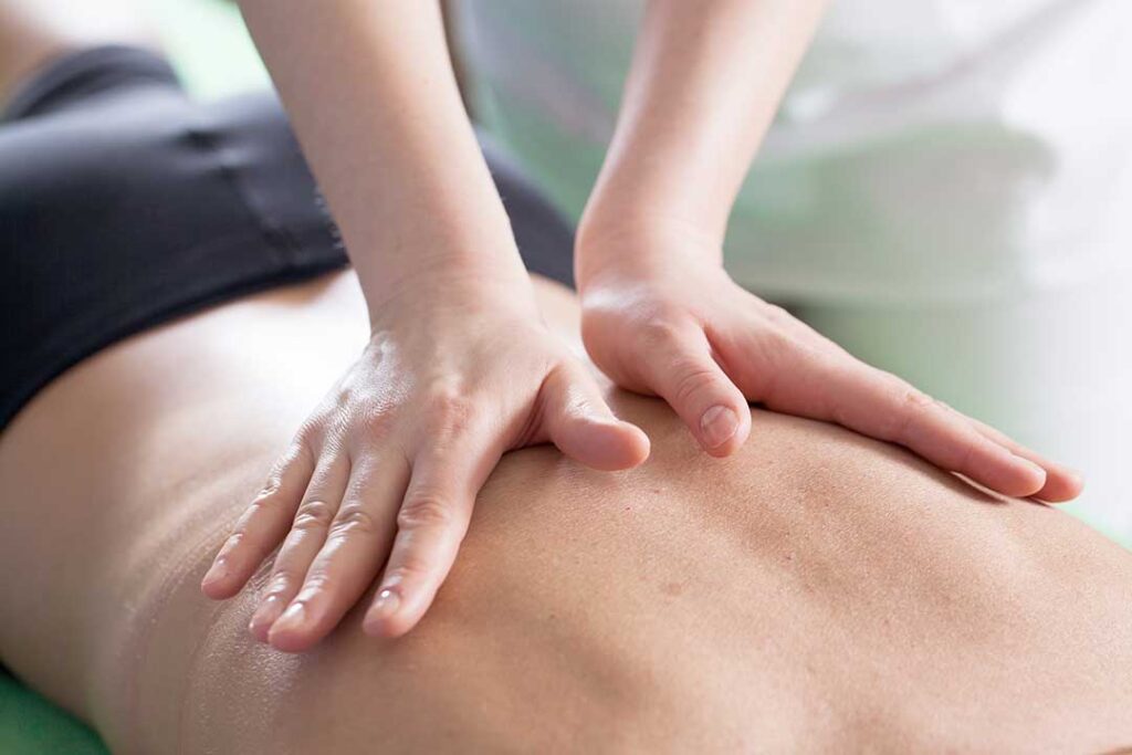 A chiropractor adjusting a young athlete’s back as they sit on a bench in athletic clothes.